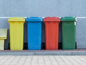 four assorted-color trash bins beside gray wall